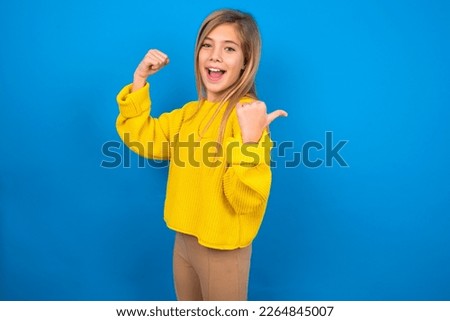 Hooray cool beautiful caucasian teen girl wearing yellow sweater over blue wall point back empty space hand fist