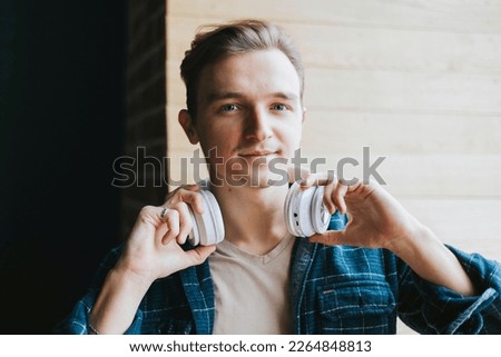 portrait of a young handsome blue eyed man with headphones in a blue shirt in front of the window