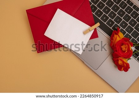 Beautiful red roses flowers in red postal envelope on neutral beige background, laptop keyboard technology online empty paper note copy space for text, spring time, greeting card for holiday. Flower 