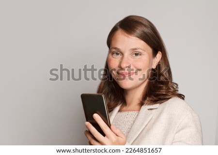 Friendly smiling woman using smartphone texting messaging friend checking social media feed browsing internet hold mobile phone against grey studio wall banner background