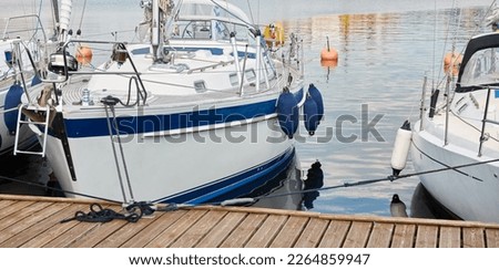White modern sailboat (for rent and sale) moored to a pier in a yacht marina. Wooden teak deck. Nautical vessel, transportation, amateur sailing, vacations, cruising, recreation concepts Royalty-Free Stock Photo #2264859947