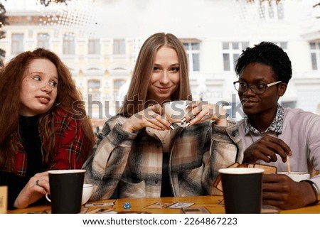 Smiling african american guy showing funny video or party photos on smartphone for diverse best friends, group of happy mixed race students meeting in cafe, laughing, sitting at table.