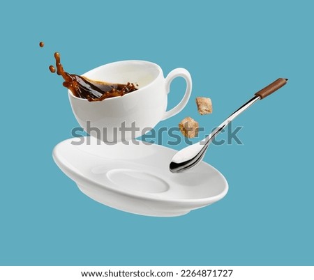 Cup of coffee with a splash drop fly with saucer and spoon isolated on blue
