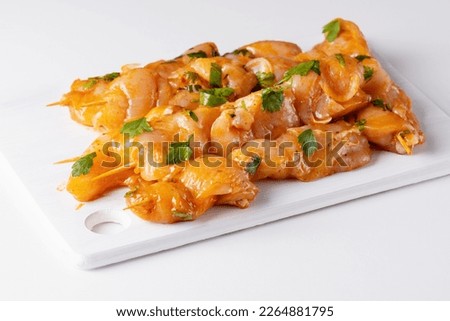 Raw chicken skewers in marinade with spices on a white board. Raw marinated and spicy chicken skewers. Chicken meat close up. Raw meat in marinade