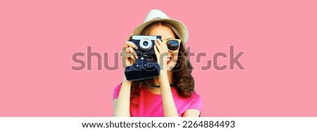 Summer portrait of young woman photographer with film camera on pink background