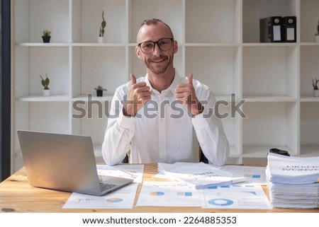 Business man at the office success sign doing positive gesture with hand, thumbs up smiling and happy. cheerful expression and winner gesture