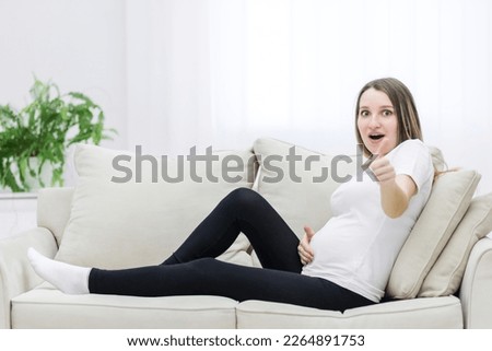 Young pregnant woman showing thumb up and looking at the camera.