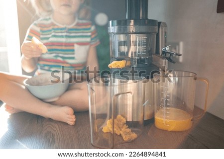 Little girl making fresh juice on the table in home kitchen. Focus on juicer. High quality photo