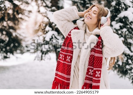 Young woman enjoying music using headphones outdoors in winter