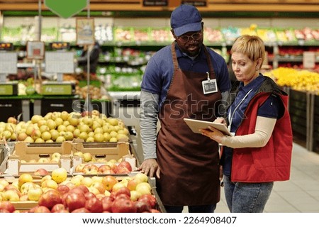 Confident mature manager of supermarket making presentation to African American male sales advisor while pointing at tablet screen Royalty-Free Stock Photo #2264908407