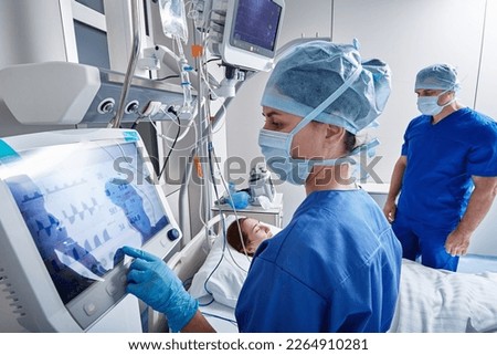 Hospital nurses checking on woman patient at intensive care unit and monitoring her health with medical equipment and sensors. ICU Royalty-Free Stock Photo #2264910281