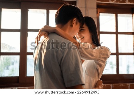 Asian young man and woman hugging each other in living room at home. Attractive romantic new marriage couple male and female spending time celebrate anniversary and valentine's day together in house. Royalty-Free Stock Photo #2264912495
