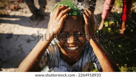 Portrait of African Little Girl Jumping and Dancing While Looking at the Camera Under Pouring Water. Happy and Innocent Black Child Playing and Enjoying the Blessing of Rain Water After Long Drought Royalty-Free Stock Photo #2264918933