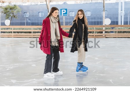 Two pretty young girls in winter clothes holding hands laughing and skating together on an ice rink
