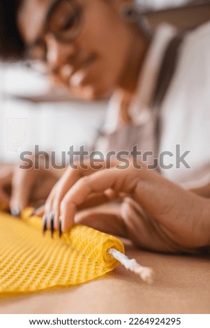 blurred african american woman rolling wax sheet while making candle in craft workshop