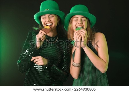 Young women in hats eating cookies on dark background. St. Patrick's Day celebration