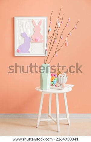 Vase with tree branches and Easter eggs on table in room