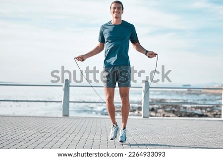 Jump rope, happy and man workout by the beach for his outdoor morning exercise, training and fitness routine. Athlete, cardio and male skipping by the ocean or sea for wellness lifestyle Royalty-Free Stock Photo #2264933093