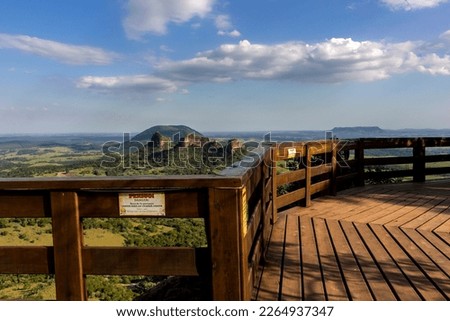 View of Três Pedras (three stones), from the Pedra do Índio viewpoint, in the city of Botucatu, Sao Paulo, Brazil. Sign written in Portuguese: danger, do not climb on the guardrail