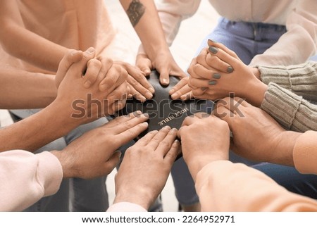 Group of people praying with Holy Bible in room, closeup