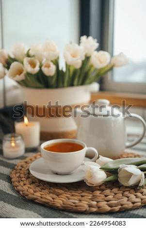 Cup of tea, teapot, basket with tulips, candles in home interior, aesthetic photo. Royalty-Free Stock Photo #2264954083