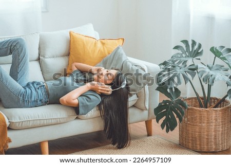 Happy woman relaxing in her sofa at home, Smiling girl is listening to music with headphones and lying down with eyes closed, Enjoy good quality sound, Stress free concept. Royalty-Free Stock Photo #2264957109