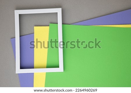 Background with a white wooden frame on green, yellow, purple sheets of paper. Flat lay. Textured background for design with empty space