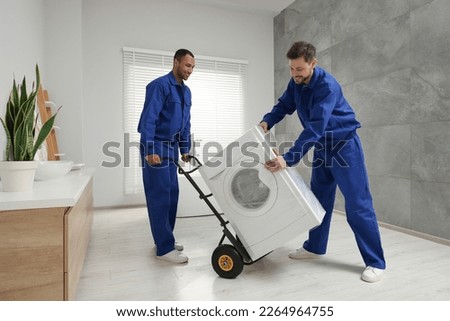 Male movers carrying washing machine in bathroom. New house Royalty-Free Stock Photo #2264964755
