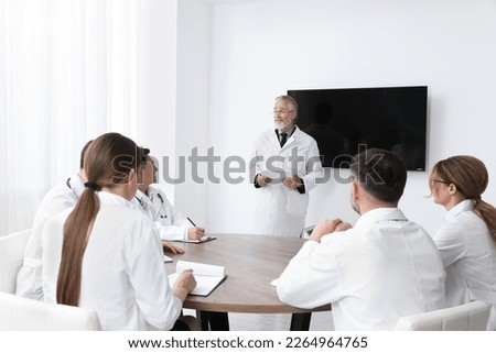 Team of doctors listening to senior speaker report near tv screen in meeting room. Medical conference