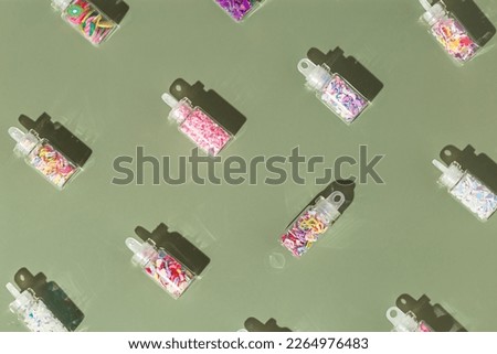 Colorful glitters diffrent form for nail art and makeup in small jars on olive green background with copyspace. Minimal aesthetic flat lay with glitter for nails in glass bottles at sunlight, top view