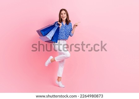 Full length photo of sweet funny lady wear print shirt holding shoppers pointing empty space isolated pink color background