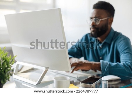 Focused african american male entrepreneur working and typing on computer keyboard, sitting at workplace in office, focus on monitor, free space