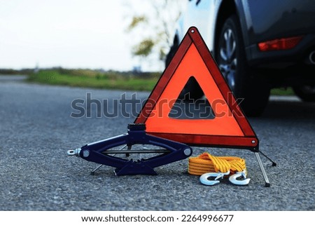 Emergency warning triangle, towing strap and scissor jack near car outdoors. Safety equipment