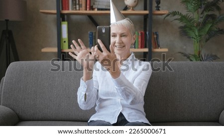 Happy business elderly woman in birthday cap talking on video call using smartphone
