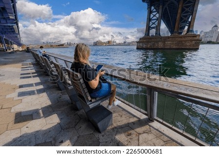 Beautiful view of Hudson River from under Brooklyn Bridge, lower Manhattan and people resting on benches. USA.