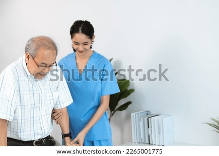 Happy smiling nurse in hospital and clinic uniform helping senior man with spectacles walk using a walker in the passage and corridor after successful treatment and physiotherapy