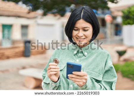 Young chinese woman using smartphone and holding bitcoin at park
