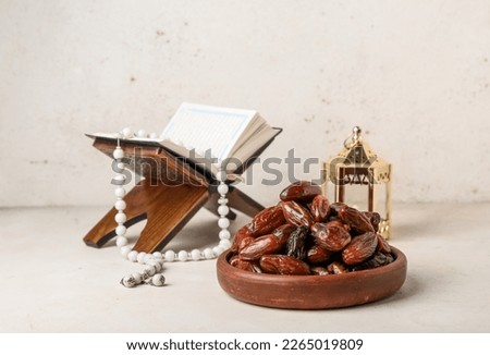 Bowl with dates, Koran and Muslim lantern for Ramadan on light background Royalty-Free Stock Photo #2265019809