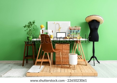Tailor's workplace with laptop, sewing machine and organizers near green wall in workshop