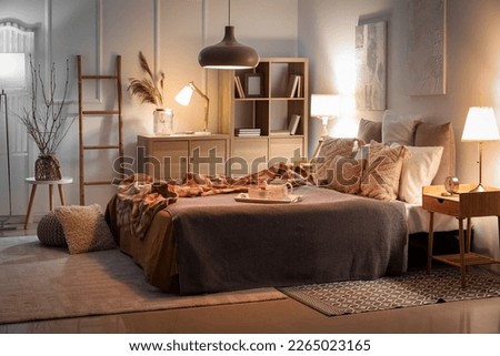 Interior of bedroom with checkered plaid on bed and glowing lamps late in evening