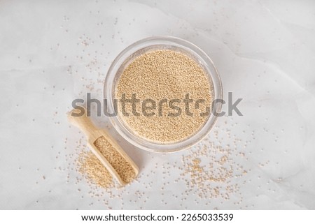 Glass and scoop of amaranth seeds on light background