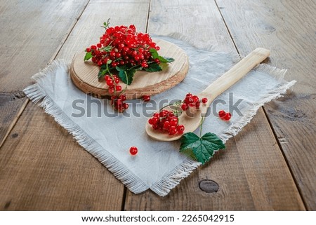 Red currants in a glass. On a wooden background, a light green napkin with leaves and red berries, on a napkin a glass transparent glass with red currant berries. High quality photo