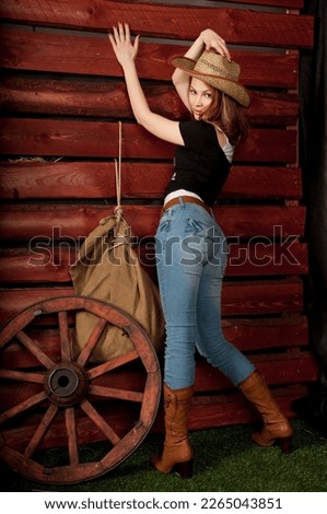 Cowgirl in a cowboy hat stands in a barn. Wagon wheel