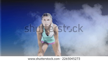Composition of blonde female athlete concentrating against clouds of smoke on blue background. sport, fitness and active lifestyle concept digitally generated image.