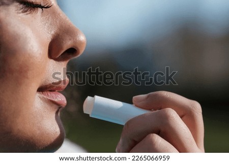 Close-up of beautiful young woman using lip balm to moisture lips. She has her eyes closed. Beauty and skin care concept. Royalty-Free Stock Photo #2265066959