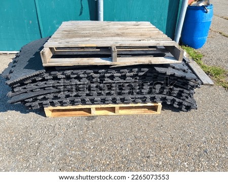 Some wooden pallets and rubber mats stacked by a building. Royalty-Free Stock Photo #2265073553