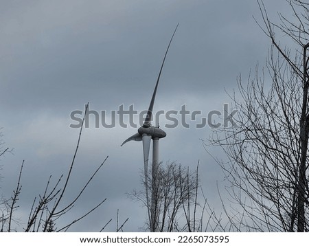 A closeup of a windmill under a cloudy sky with power lines running toward it.