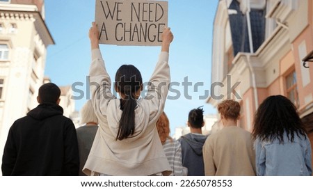 Asian woman in back of protest demonstration holding a poster We need a change. Student activist. Royalty-Free Stock Photo #2265078553