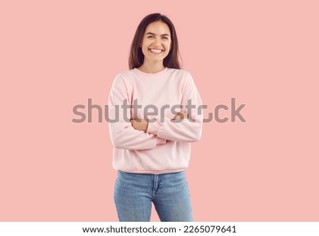Portrait of happy woman standing with her arms folded. Laughing attractive brunette girl in pink sweatshirt posing with crossed hands over isolated studio background Royalty-Free Stock Photo #2265079641