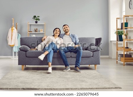 Happy smiling young couple are sitting together on cozy sofa at home in the living room, looking into the camera. Sense of harmony in relationships, care, joy, positivity, love, romance, satisfaction. Royalty-Free Stock Photo #2265079645